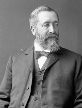Black and white photograph of William Saunders, with a well kept beard and moustache, wearing a suit and bow tie.